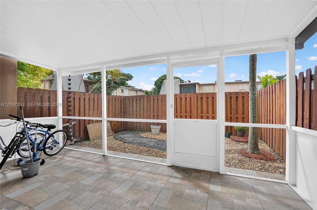 Screened-in patio with tile flooring, a white paneled ceiling, and a wooden privacy fence enclosing a gravel courtyard