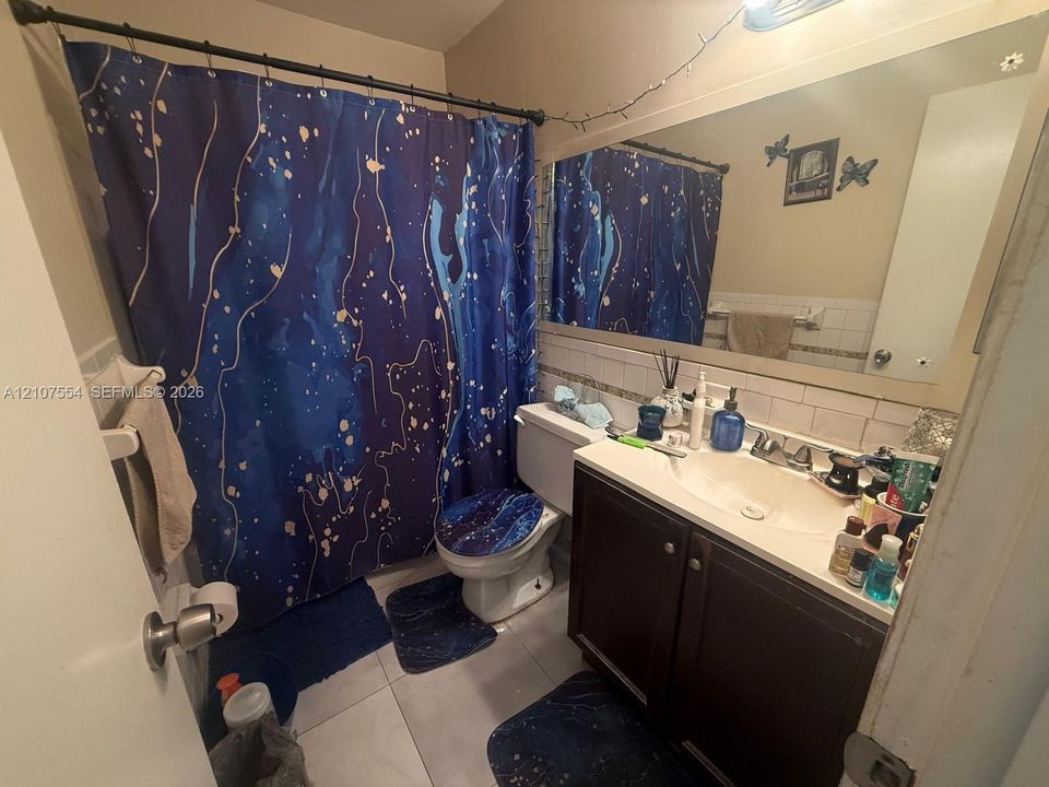 Bathroom featuring a vanity with dark-finish cabinetry, light-toned countertop, integrated basin, wall-to-wall mirror, and white tiled wall accents