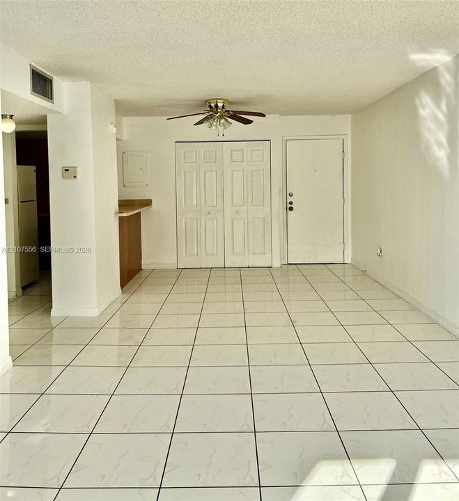 Open floor plan featuring large-format ceramic tile flooring, a central ceiling fan with integrated lighting, and white six-panel closet doors