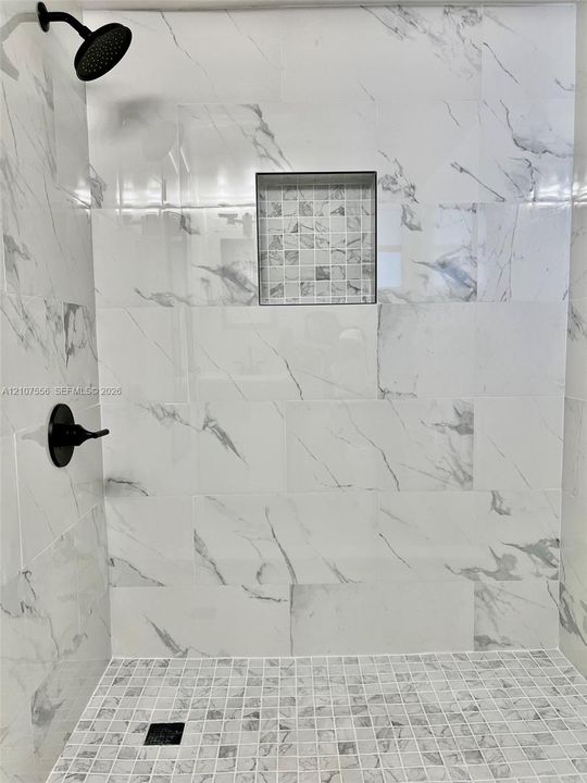 Walk-in shower featuring large-format patterned wall tile, mosaic tile flooring, a recessed storage niche, and matte black plumbing fixtures