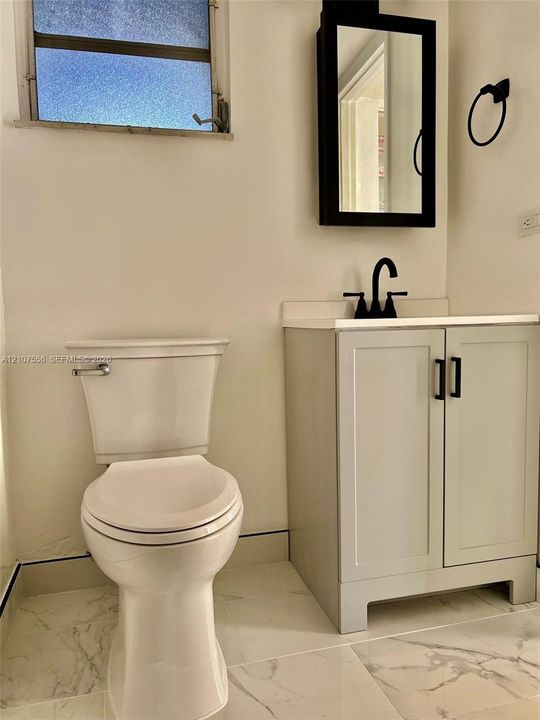 Bathroom featuring a vanity with shaker-style cabinetry, matte black hardware, a high-arc faucet, a rectangular wall-mounted mirror, and stone-finish tile flooring