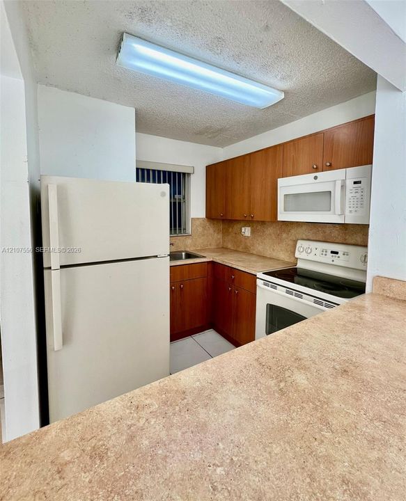 Kitchen featuring wood cabinetry, laminate countertops, a double-basin sink, and white appliances including an electric range, microwave, and refrigerator