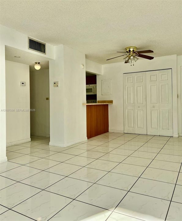 Large-format tile flooring, built-in wooden breakfast bar, ceiling fan with integrated lighting, and dual-panel closet doors