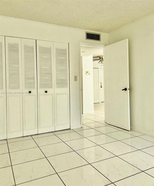 Room featuring gloss-finish tiled flooring and floor-to-ceiling closets with louvered doors
