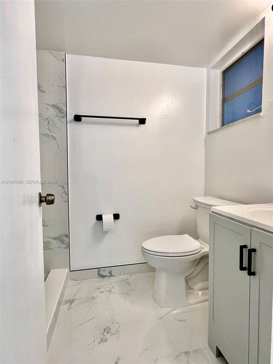 Bathroom featuring stone-pattern tile flooring, a shower surround with stone-patterned wall tile, a light gray vanity cabinet, and matte black fixtures