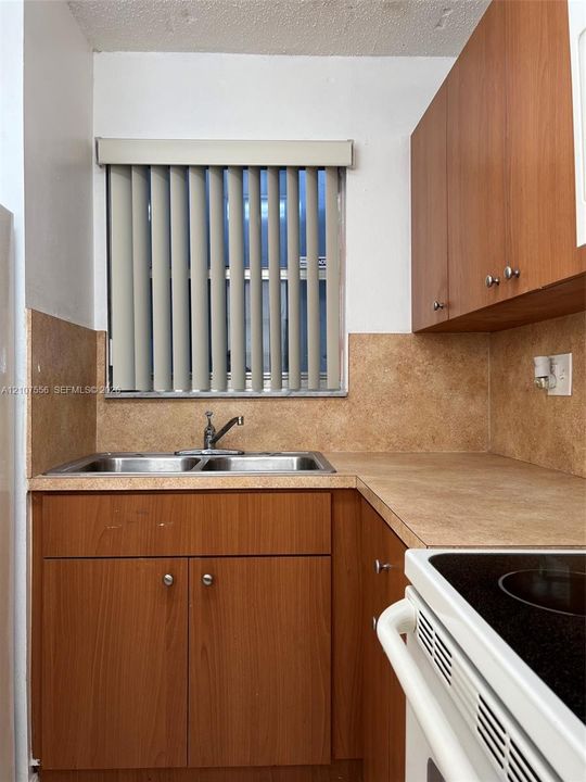 Kitchen featuring wood-finish cabinetry, a double-basin stainless steel sink, a chrome faucet, and integrated solid-surface countertops with a coordinating backsplash