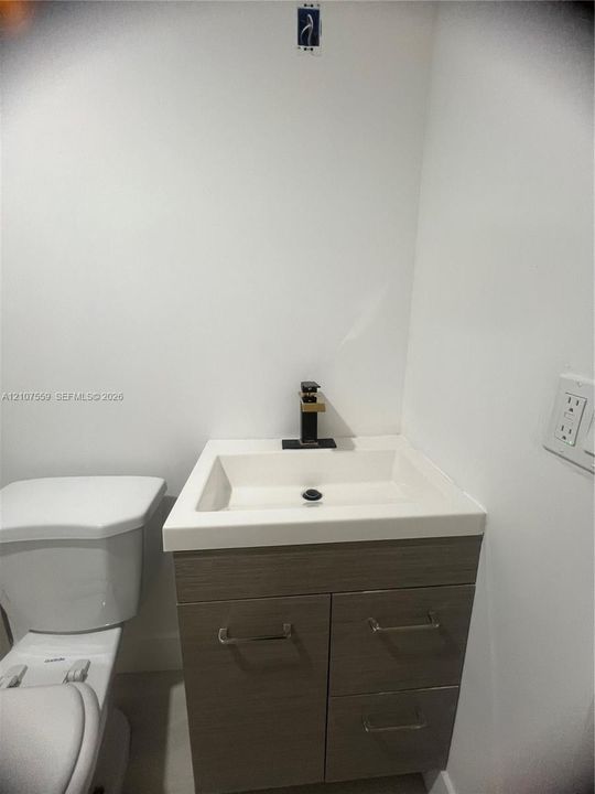 Modern vanity featuring a rectangular integrated sink, wood-finish cabinetry, and a contemporary matte black faucet