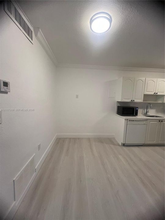 Wood-finish flooring, white cabinetry, integrated dishwasher, and stainless steel sink with high-arc faucet