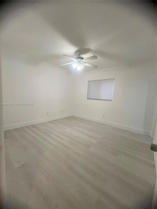 Room featuring wood-finish flooring, white walls, crown molding, and a central ceiling fan with integrated lighting