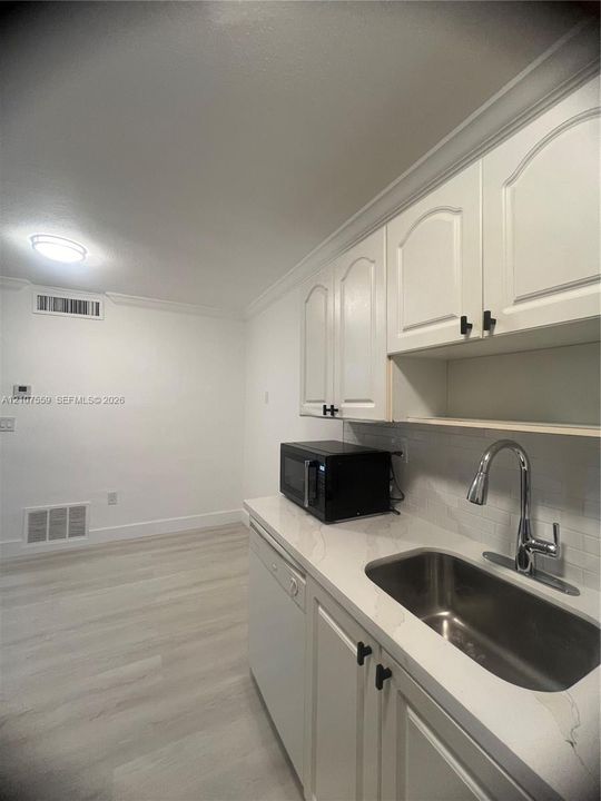 Kitchen area featuring white cabinetry with black hardware, stone-finish countertops, stainless steel undermount sink with a gooseneck faucet, and wood-finish flooring