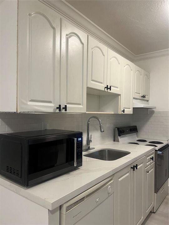 Kitchen featuring white cabinetry with matte black hardware, stone-finish countertops, white subway tile backsplash, and stainless steel sink with high-arc pull-down faucet