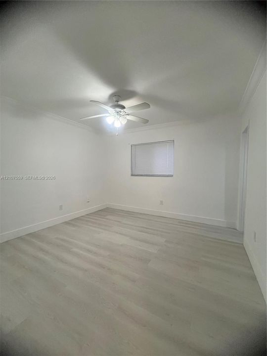 Neutral interior space featuring light-toned wood-finish flooring, crown molding, and a ceiling-mounted light fixture with a fan