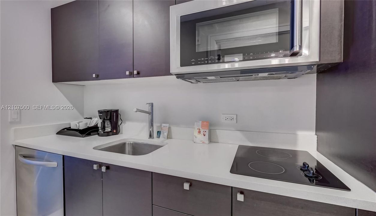 Kitchen area featuring dark cabinetry, solid surface countertops, stainless steel undermount sink, built-in microwave, and electric cooktop