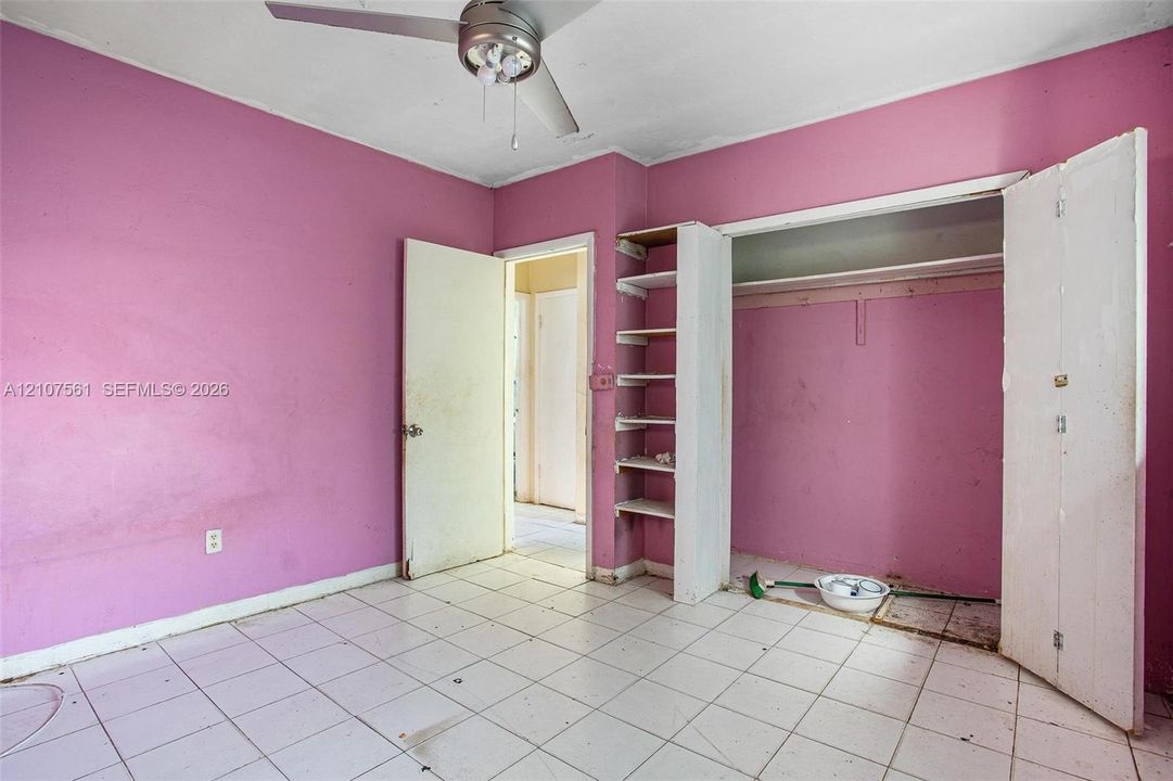 Room featuring white tile flooring, ceiling fan, and built-in wall shelving