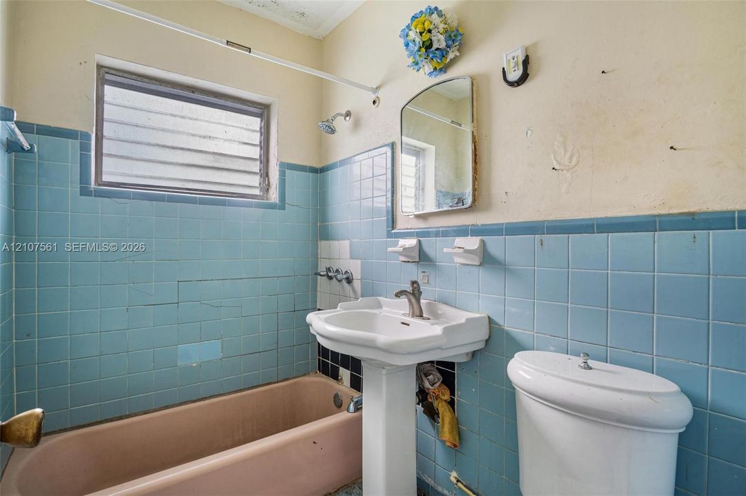 Bathroom featuring blue ceramic wall tiling, a pedestal sink with a chrome faucet, a rectangular jetted tub, and a louvered window