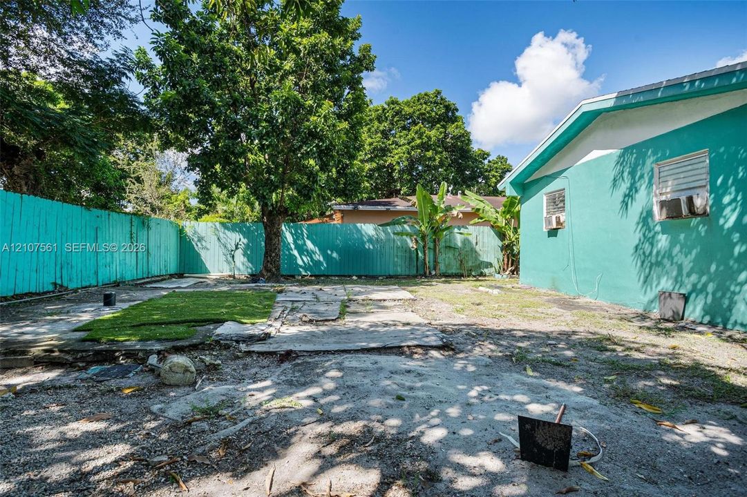 Fenced backyard featuring mature trees, partial synthetic turf, and hardscape areas
