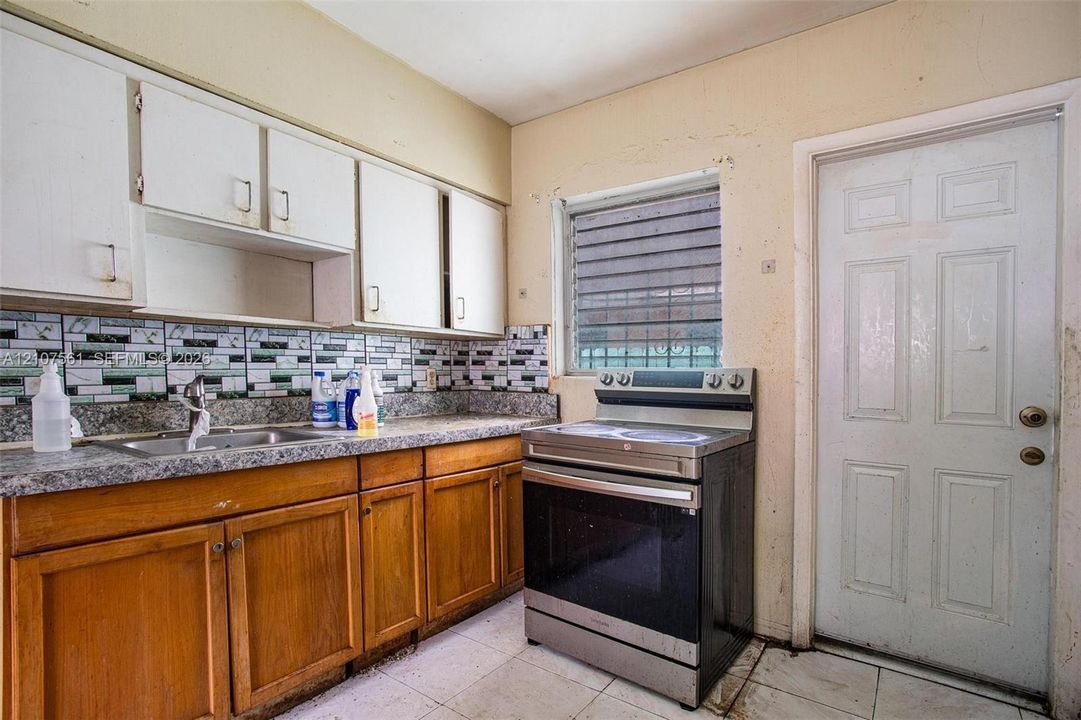 Kitchen featuring wood cabinetry, stone-finish countertops, decorative tile backsplash, stainless steel electric range, and tile flooring
