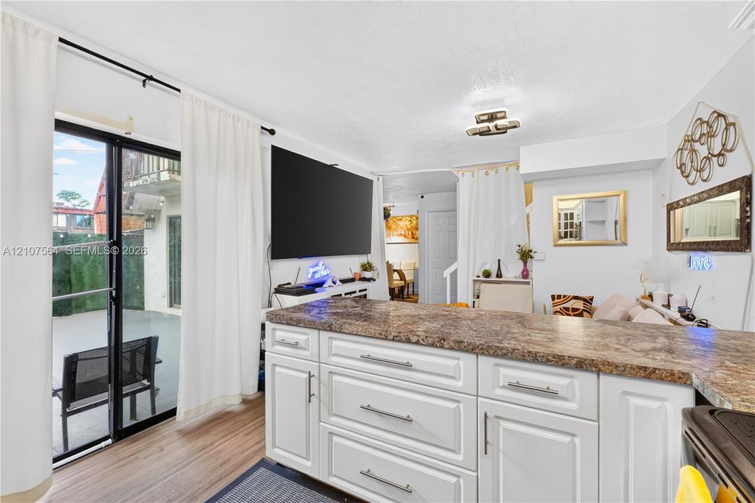 White cabinetry with integrated drawer storage, neutral stone-patterned countertop, wood-finish flooring, and sliding glass door with external access