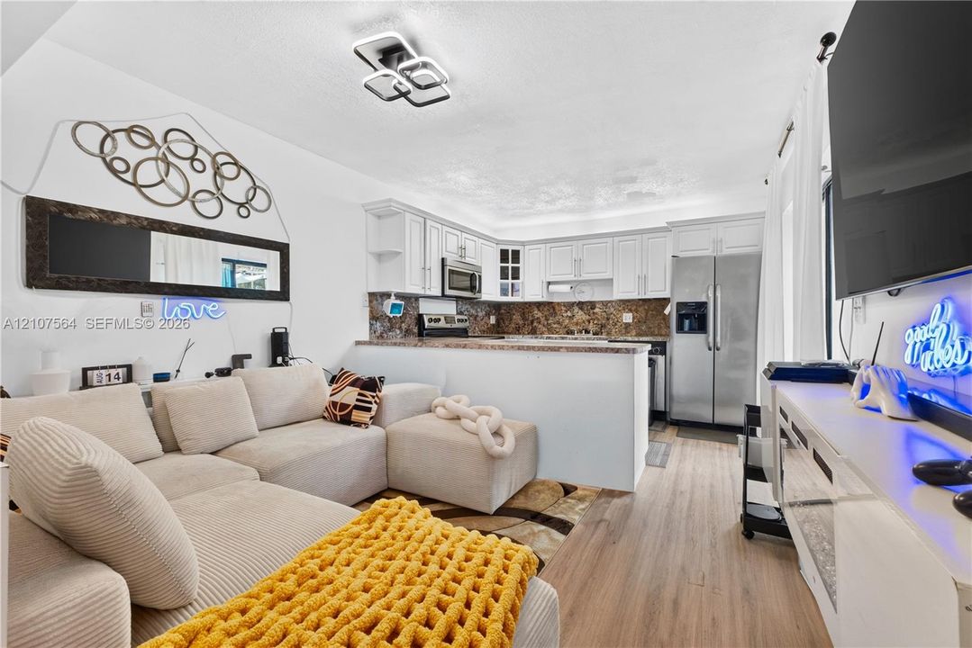 Kitchen featuring white cabinetry, stone-finish countertops, stainless steel appliances, wood-finish flooring, and a modern geometric flush-mount light fixture
