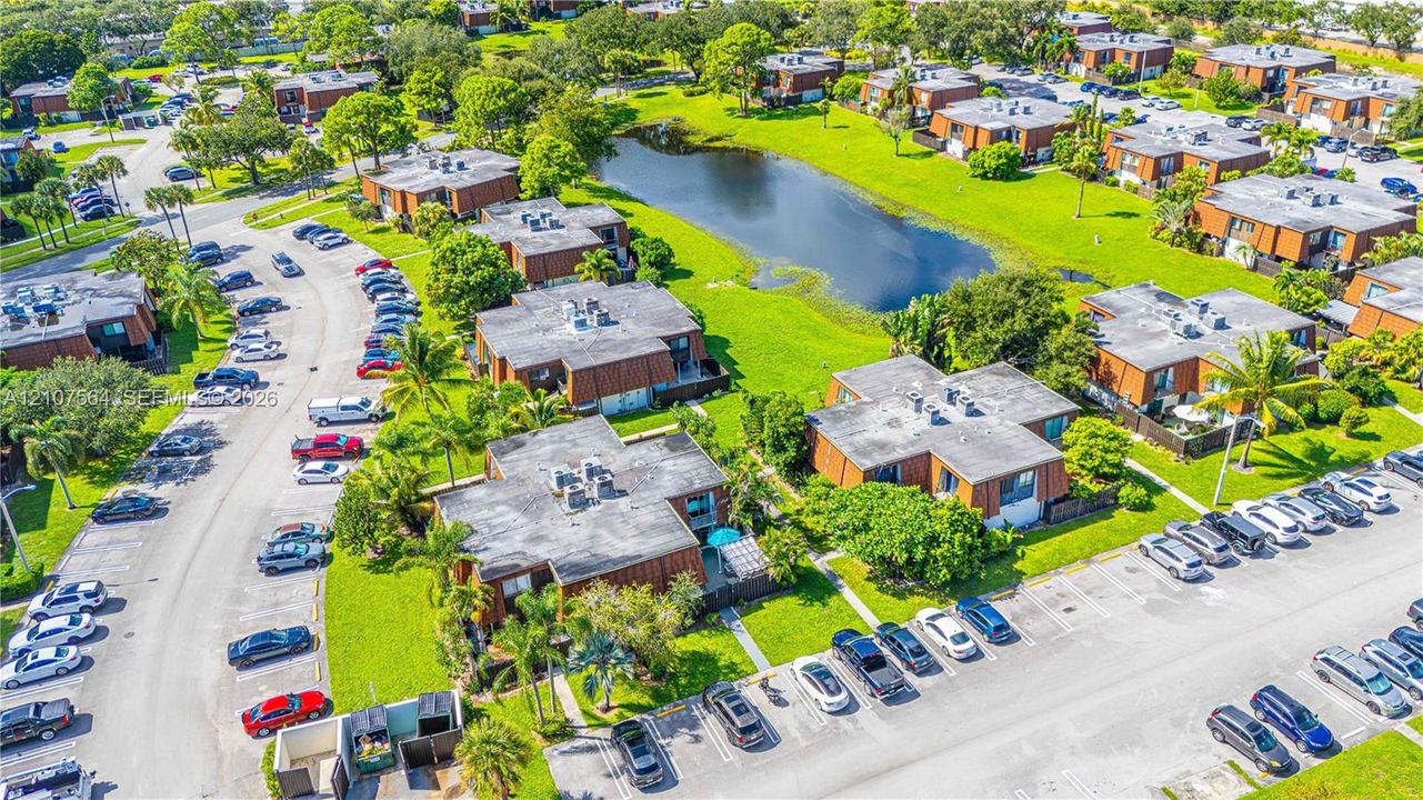Aerial perspective featuring low-rise multi-family structures, mature perimeter landscaping, central water feature, and asphalt parking lots