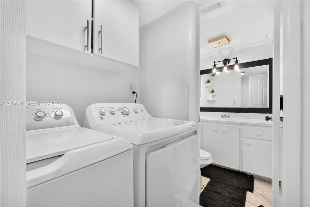 Laundry area featuring upper storage cabinetry and white cabinetry in the bathroom vanity with a framed mirror and three-light wall-mounted fixture