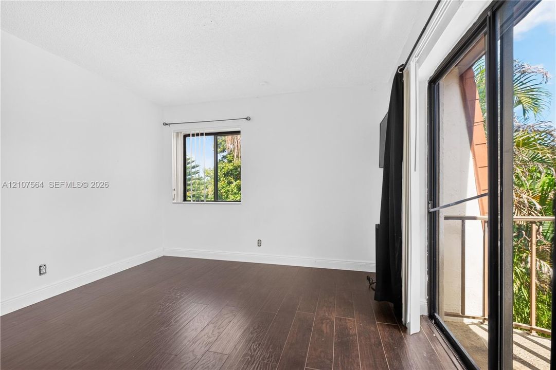 Room featuring dark wood-finish flooring, a sliding glass door, and a single window with vertical blinds