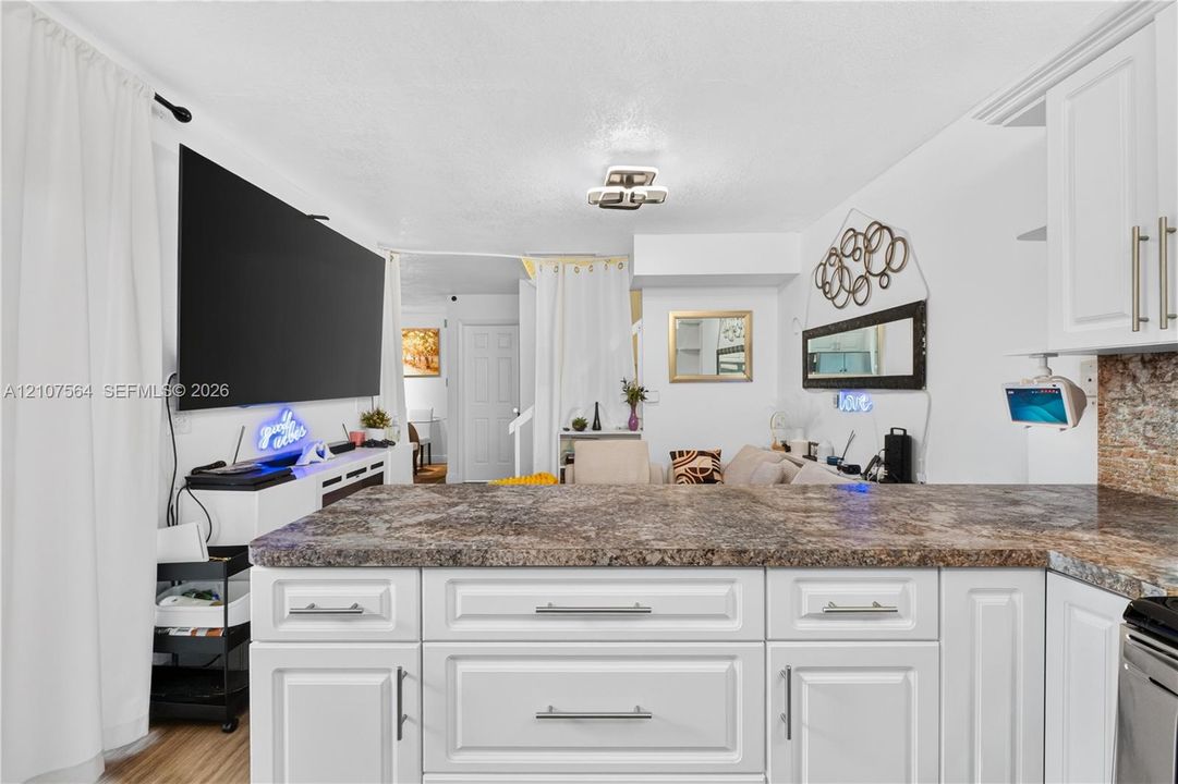 Kitchen featuring white cabinetry with brushed metal hardware, stone-finish countertops, and wood-finish flooring