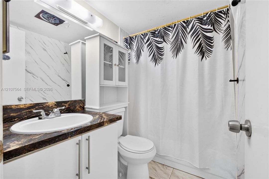 Bathroom featuring a dark stone-finish countertop, white cabinetry with silver-tone hardware, a built-in storage unit, and wall-surround tile with a veined pattern