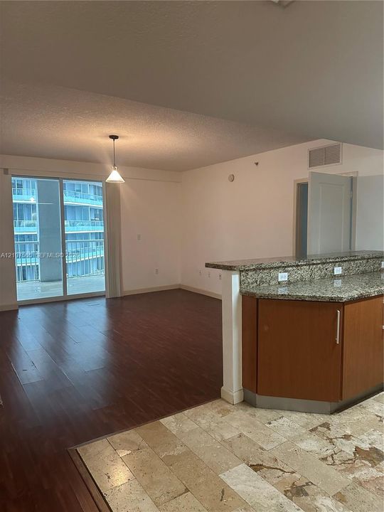 Living area featuring wood-finish flooring, stone-topped breakfast bar, cabinetry with metallic pulls, and sliding glass doors