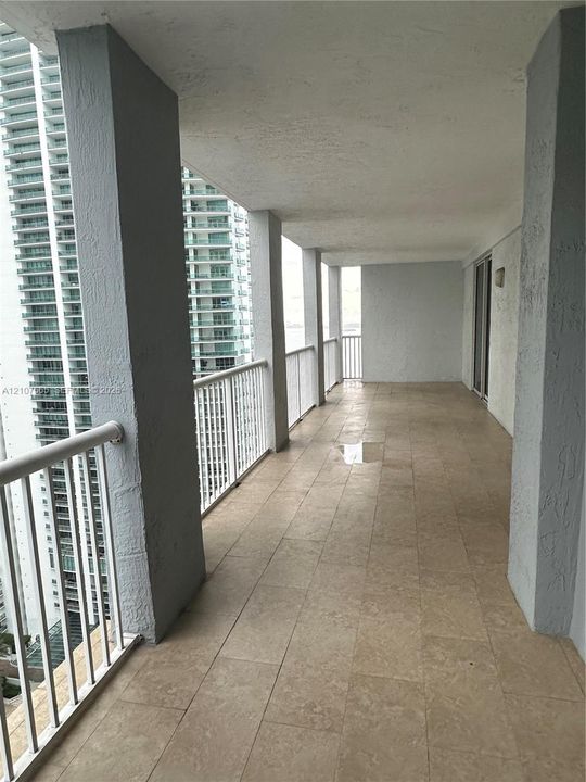 Covered balcony featuring stone-finish tile flooring, textured structural columns, and white metal railings