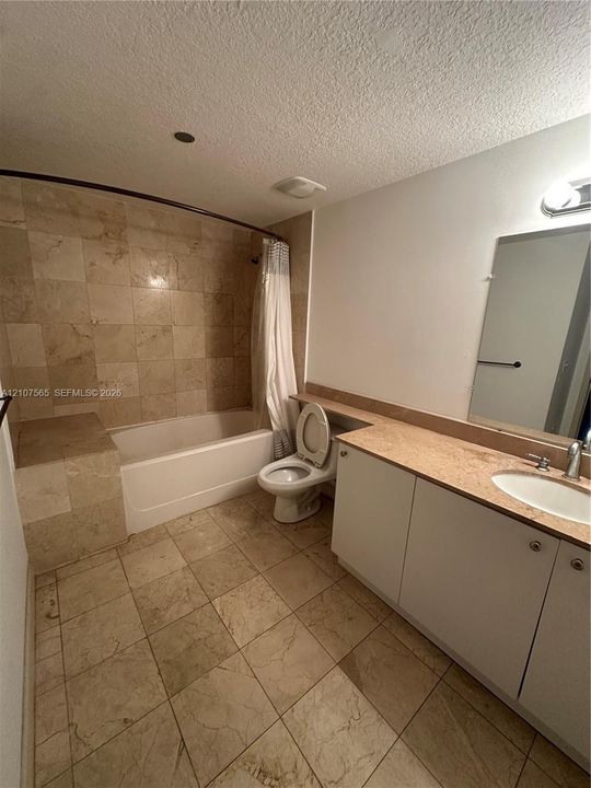 Bathroom featuring natural stone tile flooring, a tub-shower combination with floor-to-ceiling stone tile surround, a built-in tiled tub bench, and a vanity with a stone countertop