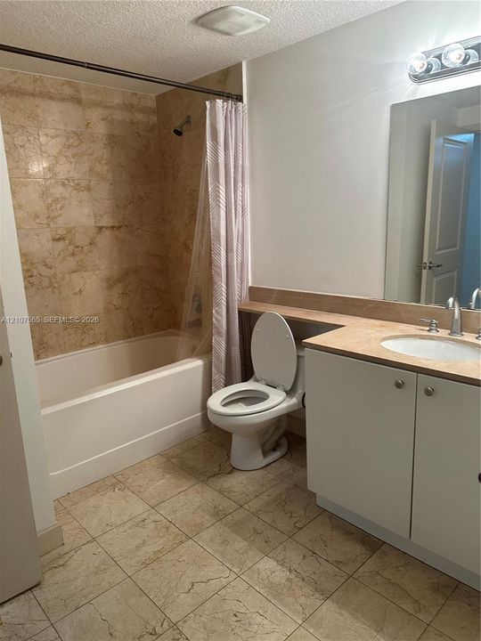 Bathroom featuring a stone-tile bathtub surround, stone-tile flooring, vanity with a stone countertop, an integrated sink, and a wall-mounted vanity light