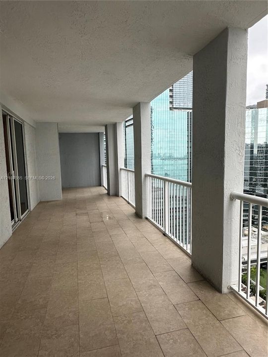 Covered outdoor balcony featuring neutral-toned tile flooring, white vertical metal railing, and concrete structural columns