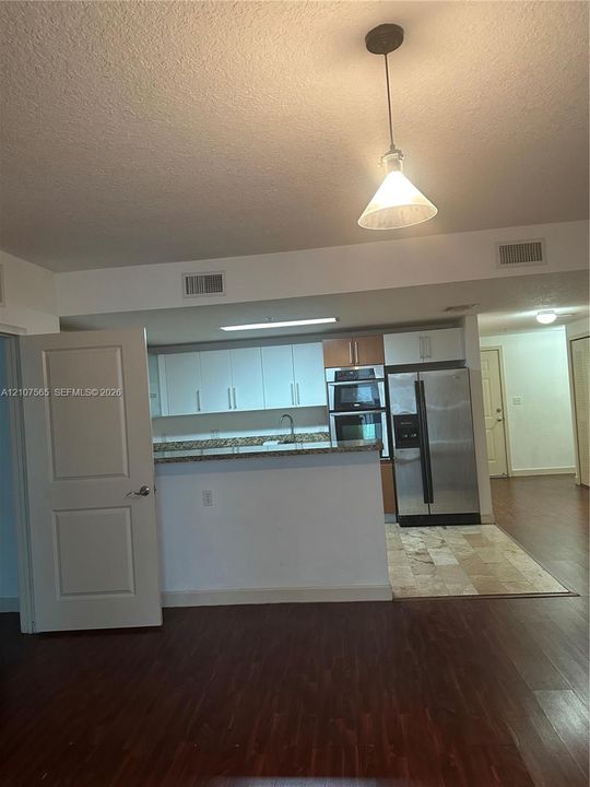 Kitchen featuring white cabinetry, stone-finish countertops, built-in double wall ovens, stainless steel refrigerator, and pendant lighting