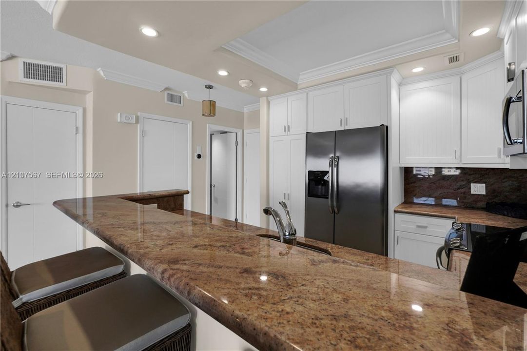 Kitchen featuring a stone breakfast bar, white cabinetry, stainless steel appliances, recessed ceiling lighting, and crown molding
