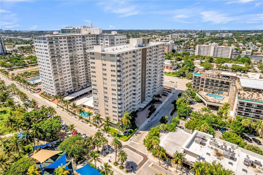 High-rise residential building featuring private balconies, ground-level surface parking, mature palm trees, and an outdoor swimming pool