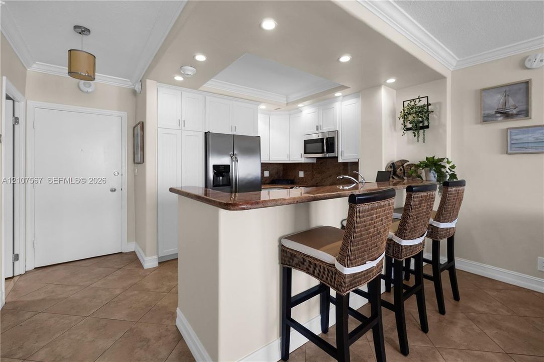 Kitchen featuring white cabinetry, stone countertops, a breakfast bar, recessed ceiling lighting, and tile flooring