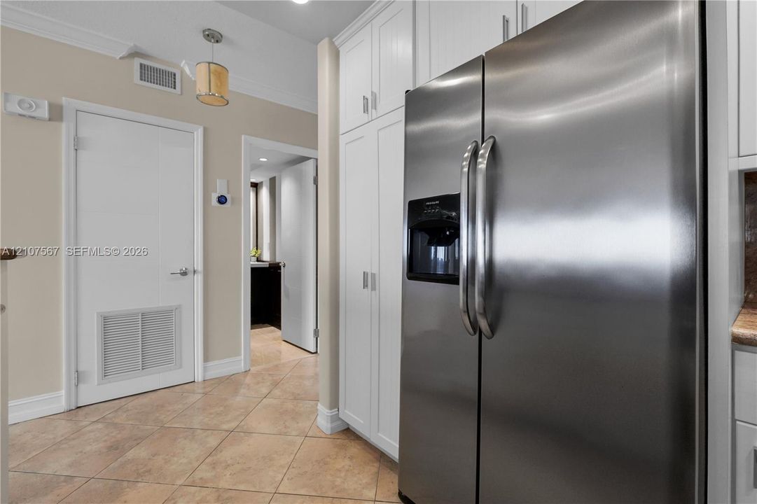 Stainless steel side-by-side refrigerator, full-height white built-in cabinetry, and ceramic tile flooring