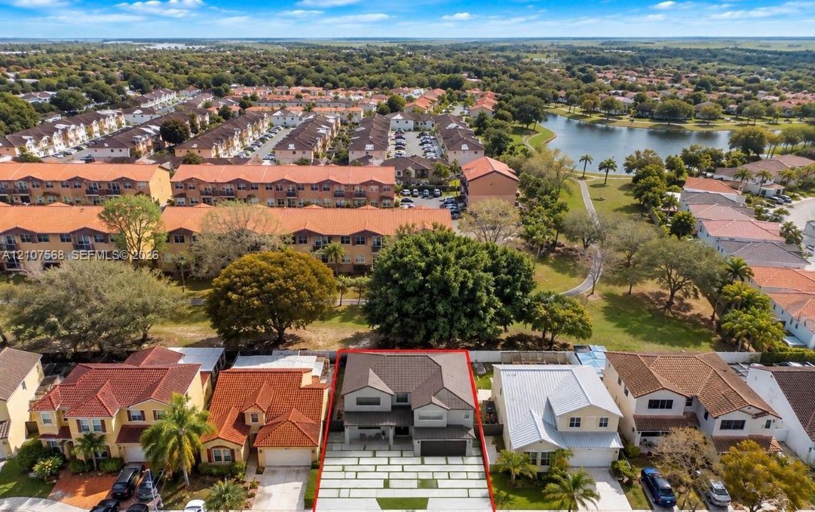 Aerial perspective of a multi-level residence featuring a multi-pitched roofline, an attached two-car garage, and a linear paver driveway with integrated turf accents