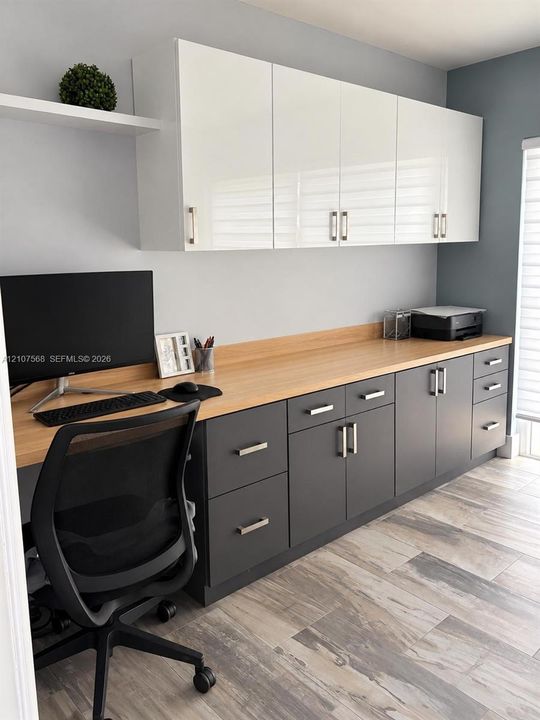 Custom cabinetry featuring high-gloss white upper units and matte charcoal base cabinets, light-toned wood-finish countertop, and durable ceramic tile flooring
