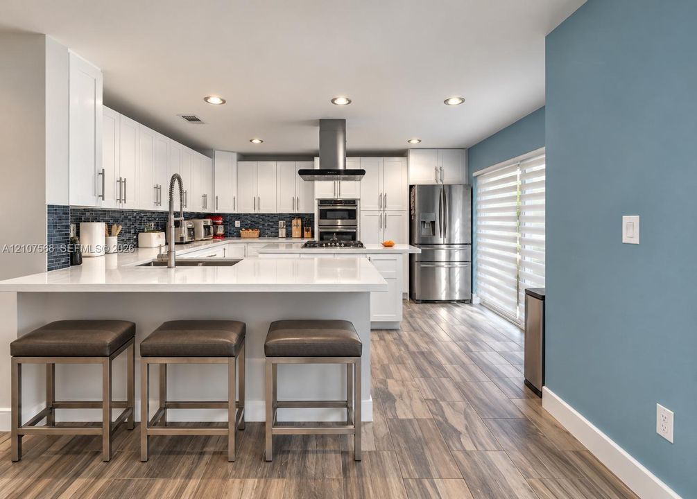 Kitchen featuring white cabinetry, quartz countertops, a stainless steel range hood, built-in stainless steel appliances, and wood-finish flooring
