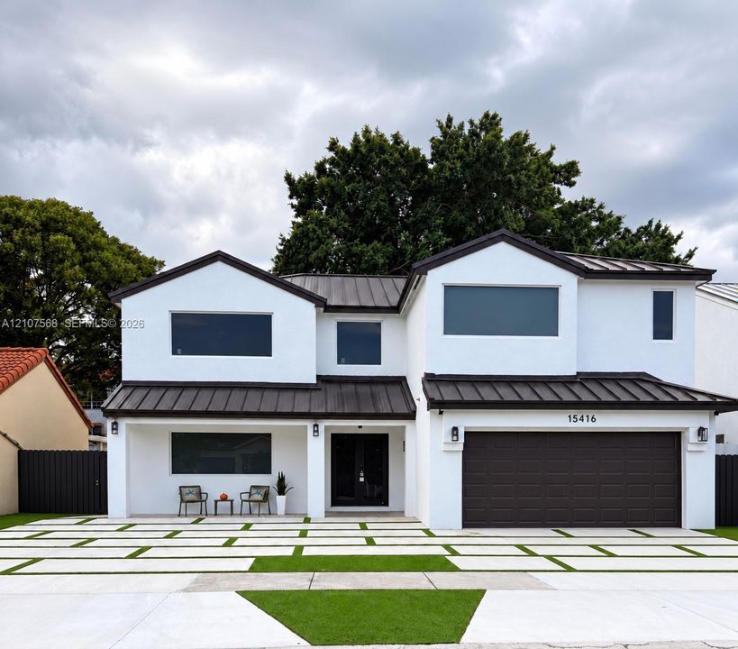 Two-story exterior featuring white stucco finish, dark metal roofing, integrated multi-car garage, and geometric concrete paver driveway with turf accents