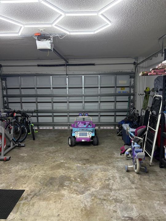 Attached garage featuring a multi-panel steel door, ceiling-mounted automatic door opener, and hexagonal geometric LED lighting