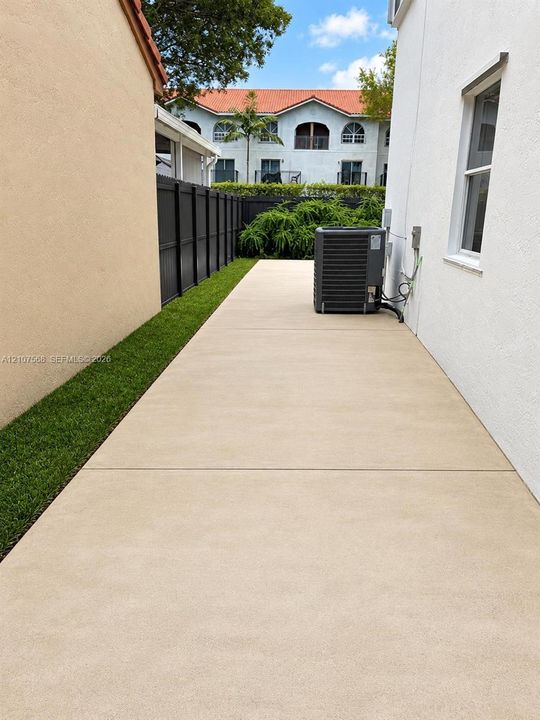 Side yard featuring a concrete walkway, synthetic turf border, and privacy fencing