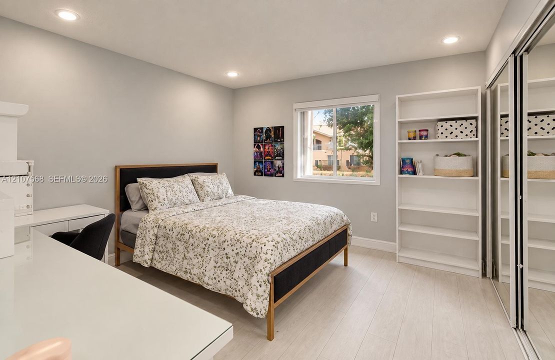 Bedroom featuring light-toned wood-finish flooring, recessed lighting, built-in shelving, and a mirrored sliding-door closet