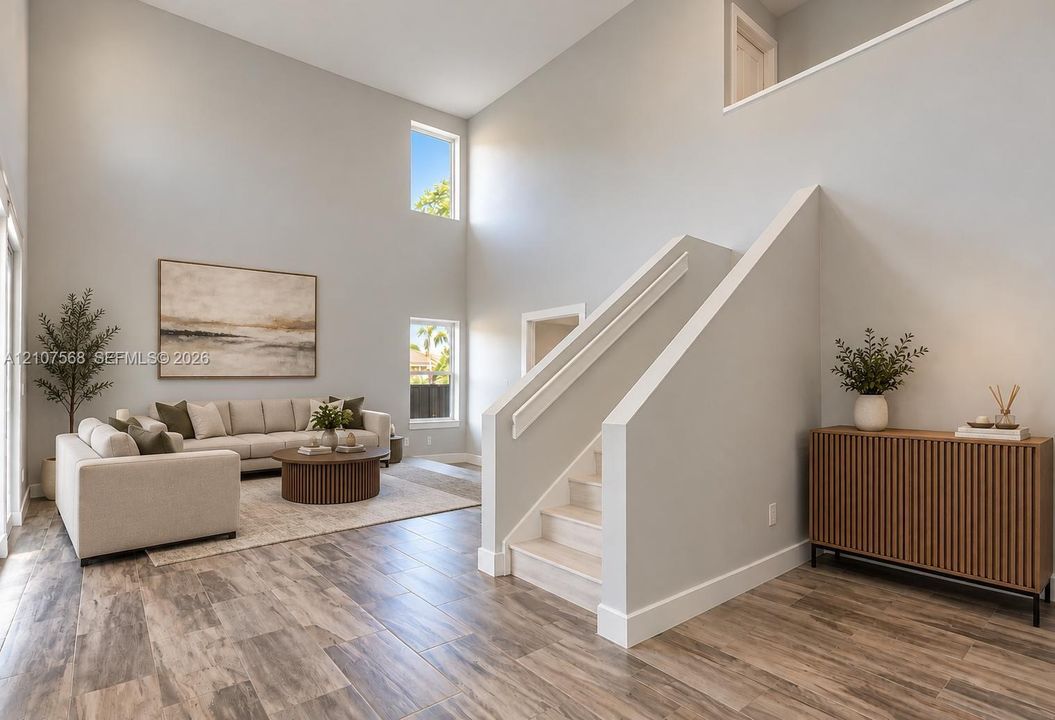 High-ceiling interior featuring double-height windows, wood-finish flooring, and a staircase with a solid-panel railing