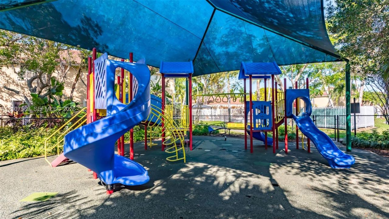 Recreational area featuring a multi-structure play system, dual slides, monkey bars, and a large overhead shade canopy