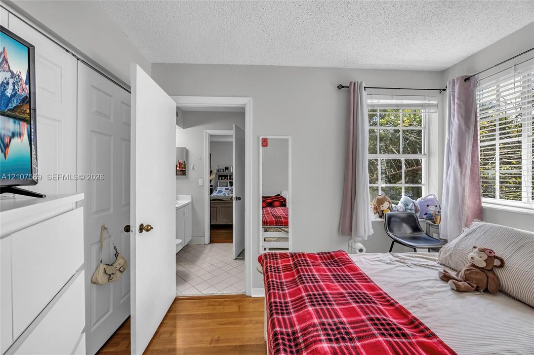 Bedroom featuring wood-finish flooring, multi-panel sliding closet doors, and a multi-pane window with horizontal blinds