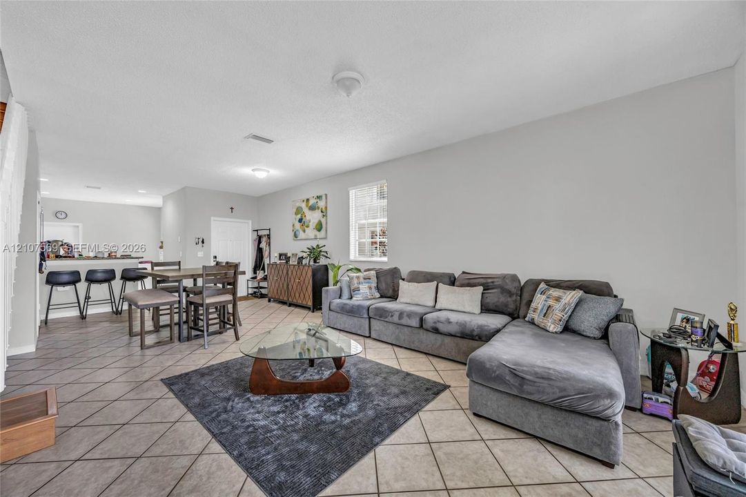 Open-concept interior featuring neutral wall tones, large-format tile flooring laid on the diagonal, and a breakfast bar