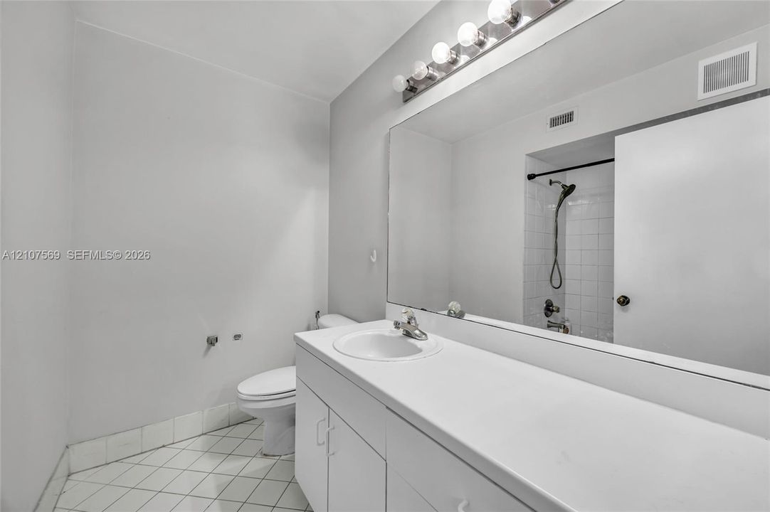 Bathroom featuring a white vanity with a solid-surface countertop, an expansive wall-to-wall mirror, an integrated sink with a chrome faucet, and tile flooring